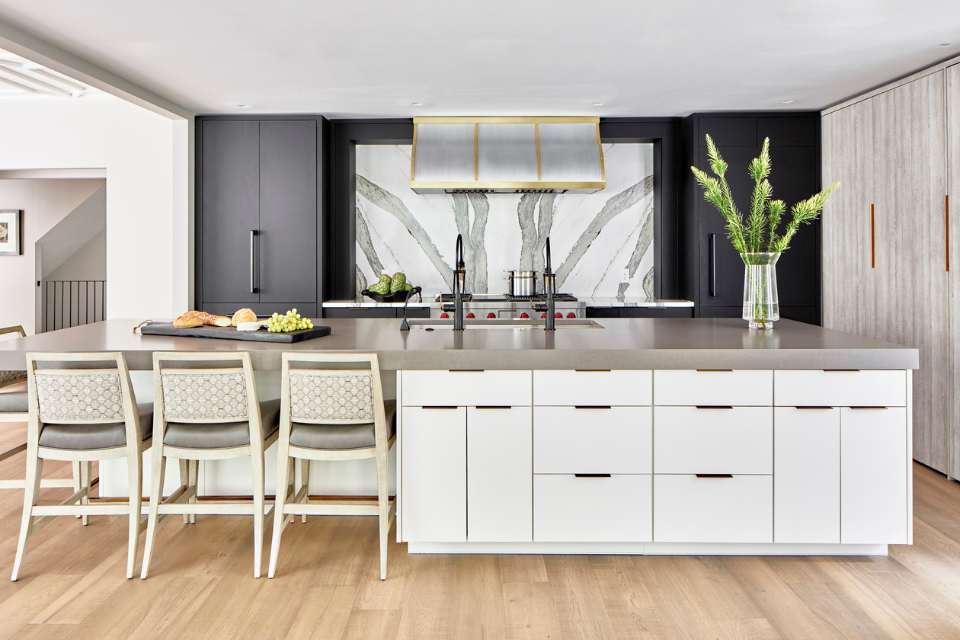 designer kitchen in modern home with white marble backsplash, black cabinetry and statement oven hood